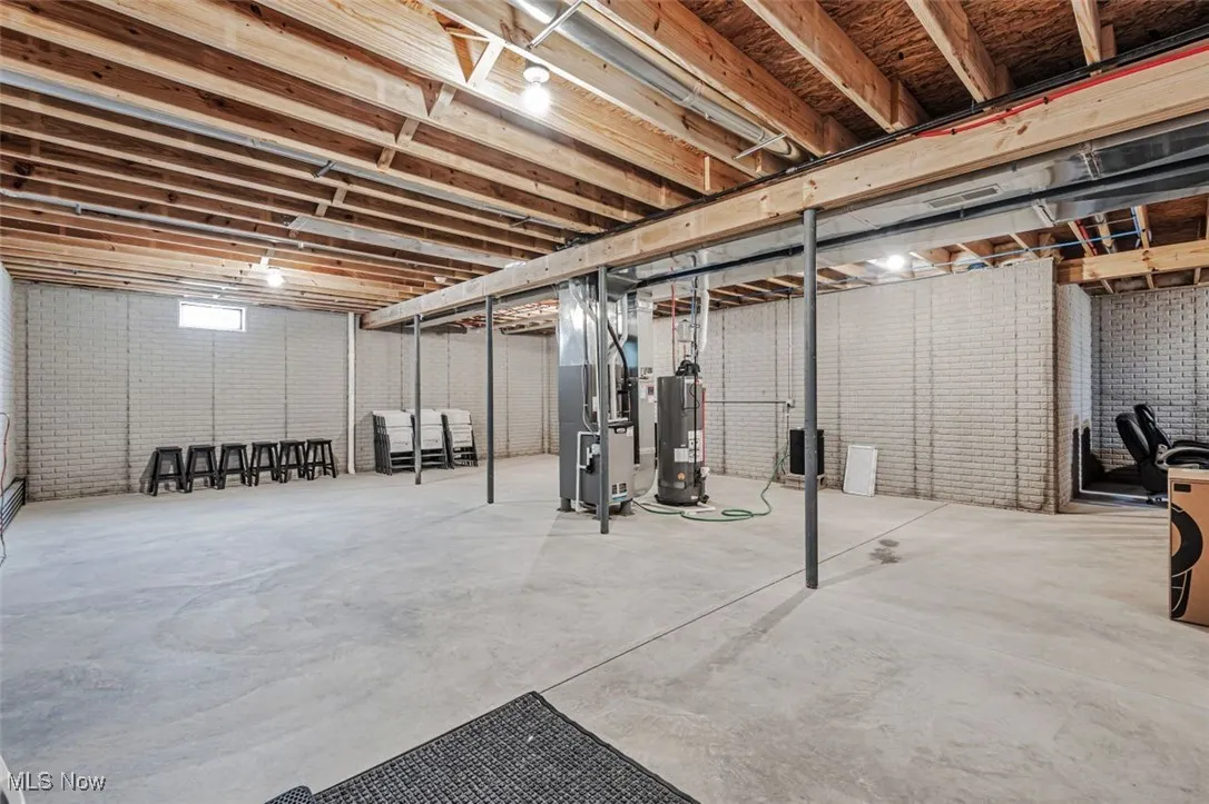 Unfinished basement with gas water heater, heating unit, and brick wall