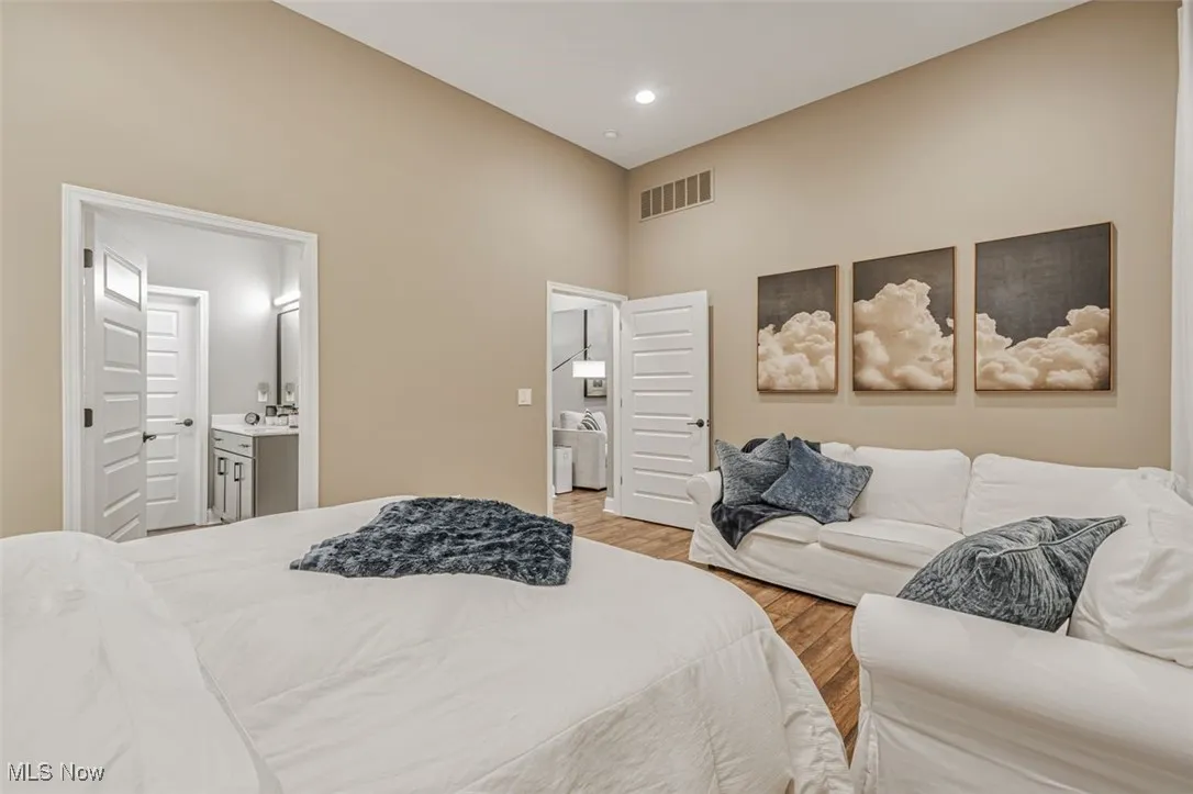 Bedroom with light wood-type flooring, a high ceiling, and connected bathroom
