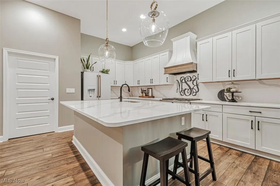 Kitchen featuring premium range hood, white refrigerator with ice dispenser, a sink, light wood finished floors, and white cabinetry