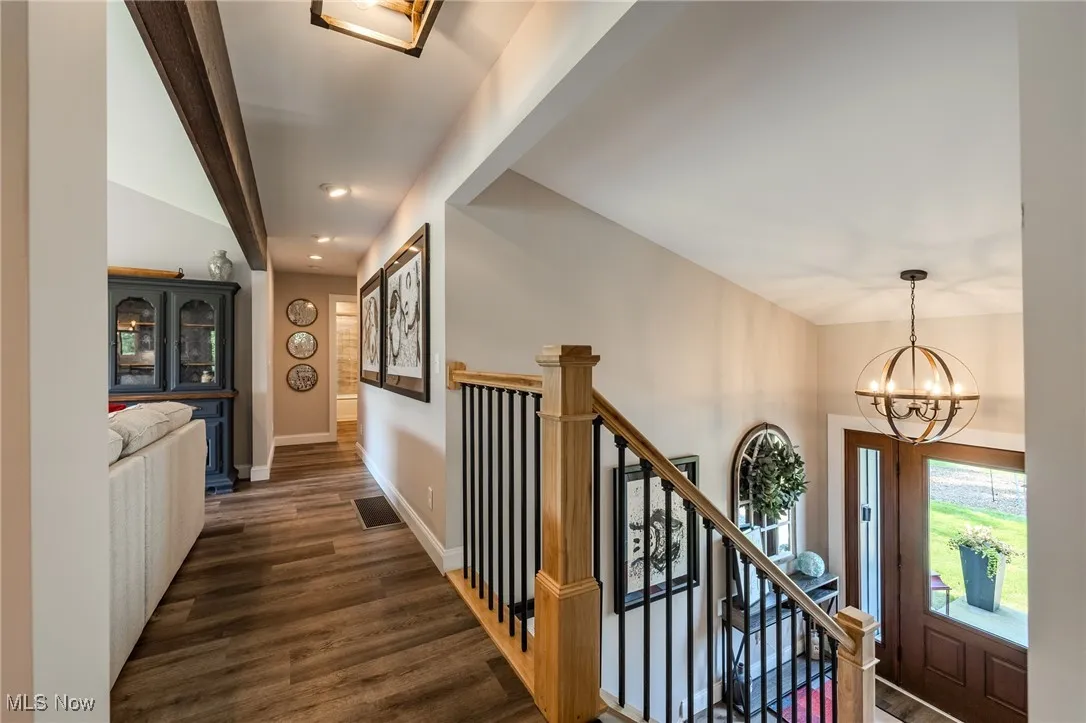 Hallway featuring dark wood finished floors, a chandelier, lofted ceiling, baseboards, and stairway