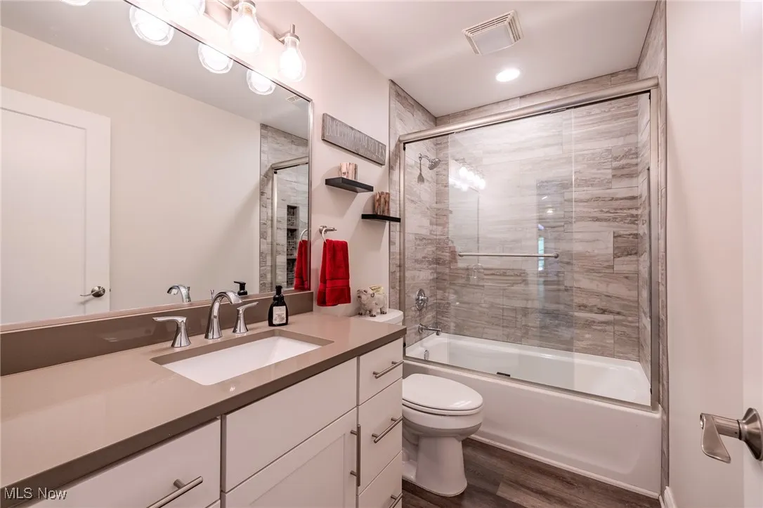 Ensuite  bath with toilet, wood finished floors, vanity, and enclosed tub / shower combo