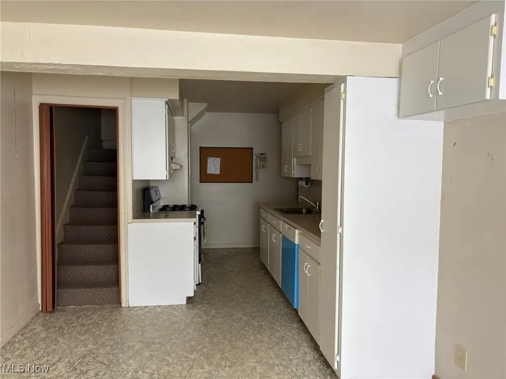 Kitchen with gas stove, a sink, dishwasher, light flooring, and baseboards