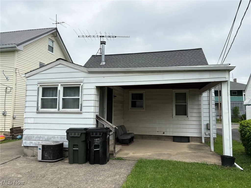 Rear view of property with cooling unit, entry steps, roof with shingles, and a patio area