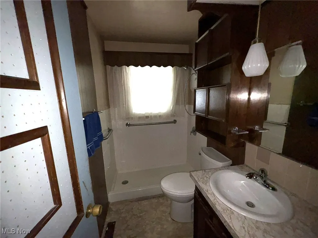 Bathroom with a shower stall, toilet, vanity, and tasteful backsplash