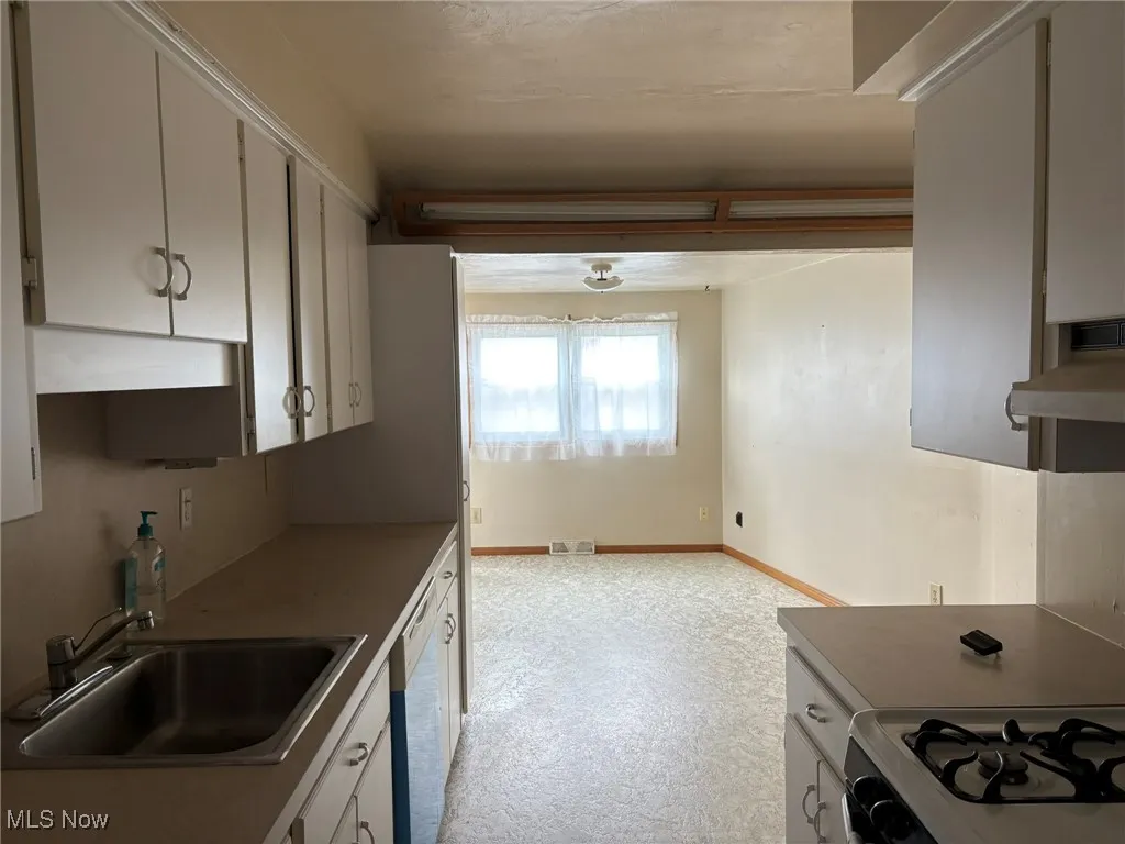 Kitchen featuring a sink, ventilation hood, white appliances, baseboards, and white cabinets