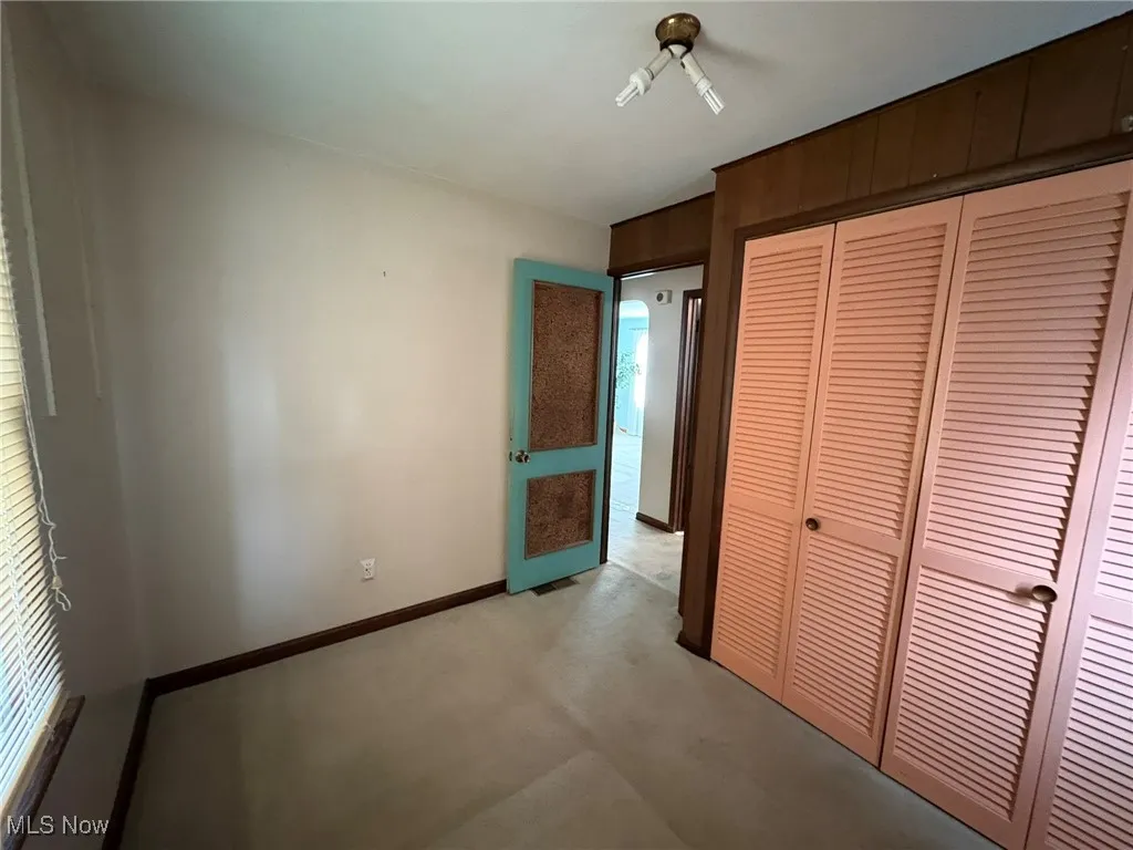Unfurnished bedroom featuring a closet, light colored carpet, and baseboards