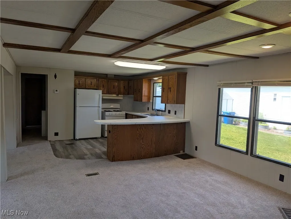 Kitchen featuring white appliances, a peninsula, light countertops, and light carpet