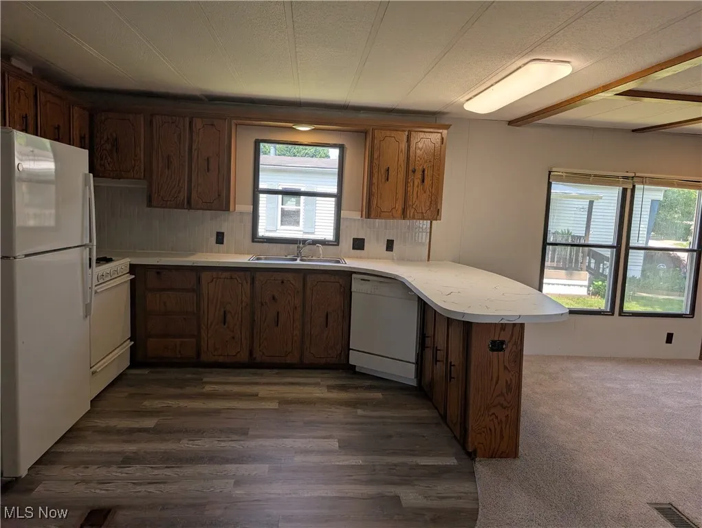 Kitchen featuring white appliances, a peninsula, light countertops, a sink, and dark wood-type flooring