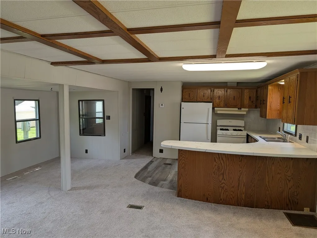 Kitchen with white appliances, under cabinet range hood, a sink, light countertops, and a peninsula