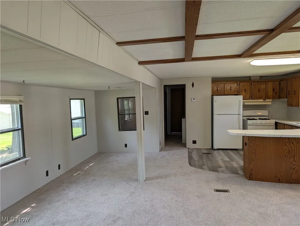Kitchen with white appliances, open floor plan, light carpet, light countertops, and under cabinet range hood