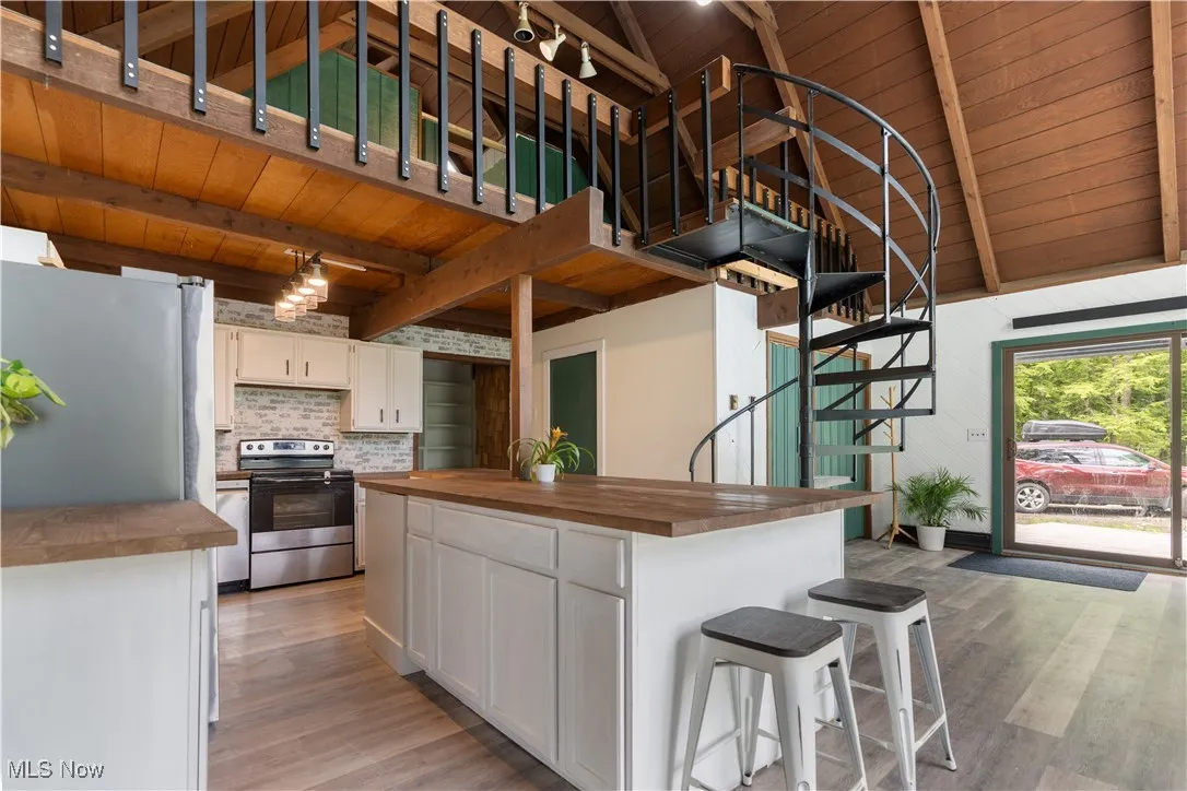 Kitchen with stainless steel appliances, butcher block counters, wood ceiling with exposed beams, light wood-style floors, and white cabinetry