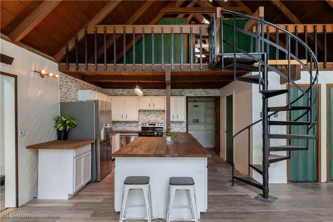 Kitchen with stainless steel appliances, butcher block countertops, wood finished floors, white cabinetry, and wooden ceiling