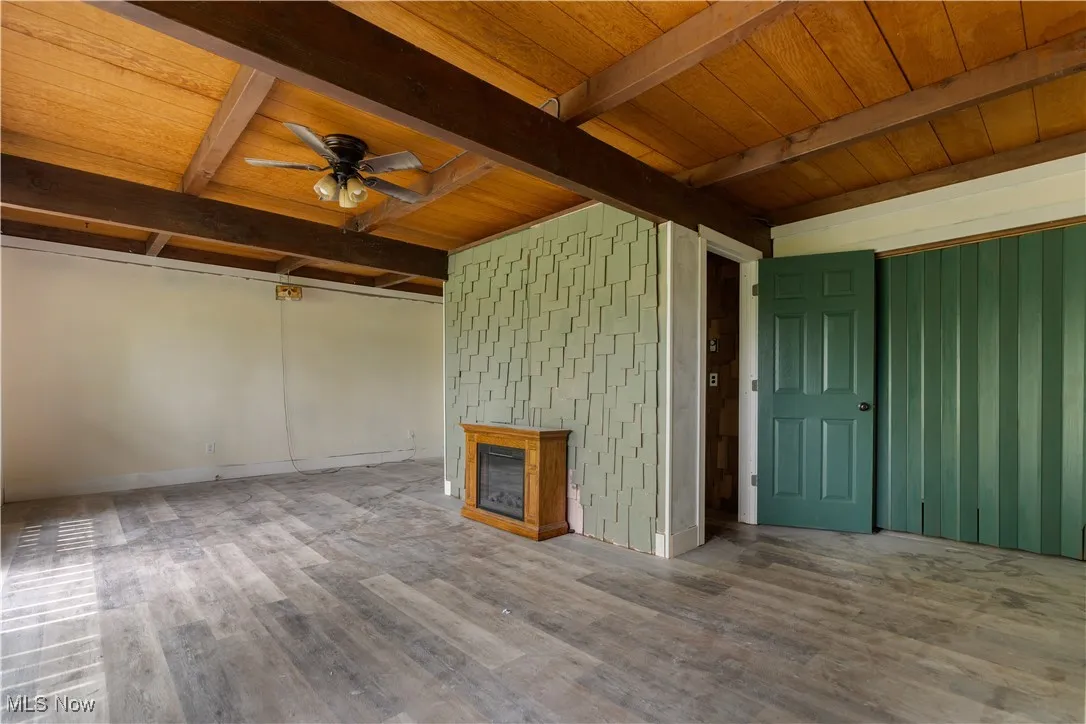 Unfurnished living room with wood finished floors, ceiling fan, a fireplace, and wood ceiling with exposed beams