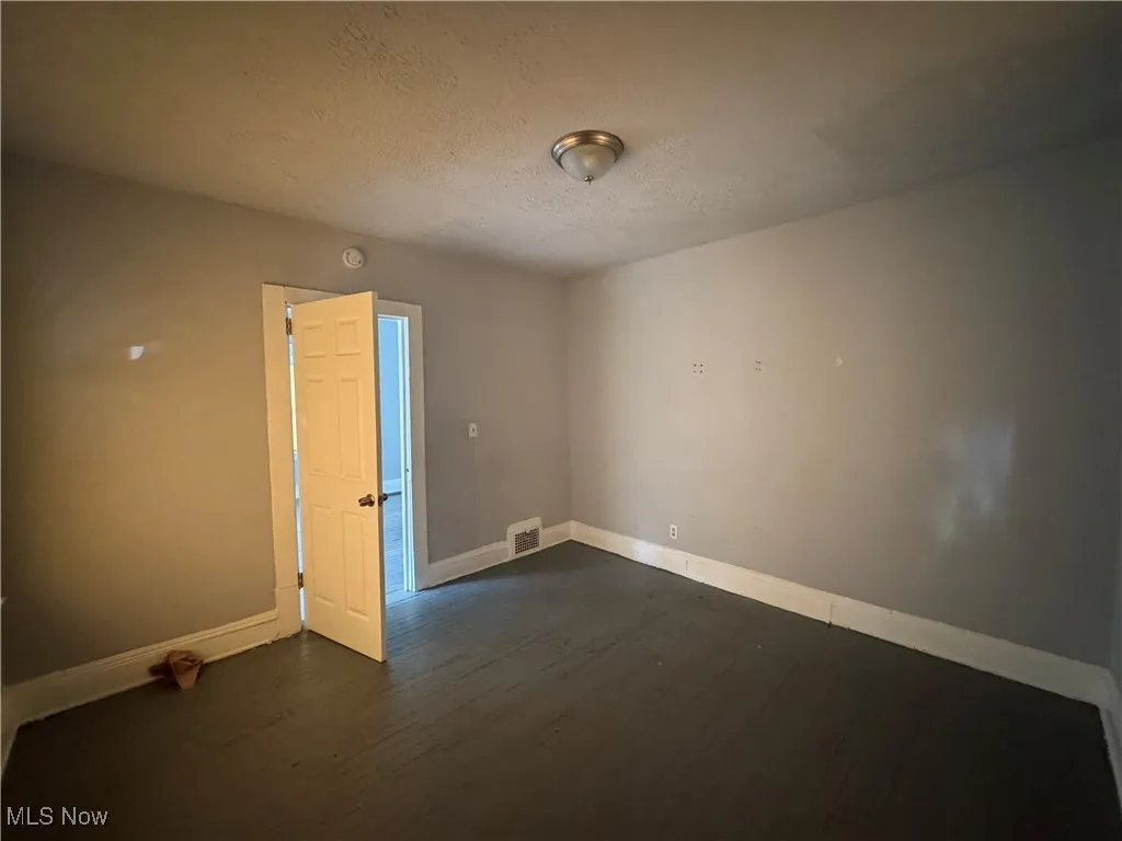 Empty room with a textured ceiling and dark wood-style flooring