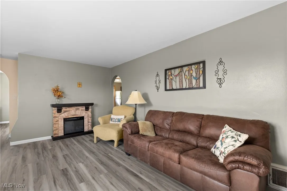 Living room with arched walkways, wood finished floors, a stone fireplace, and baseboards