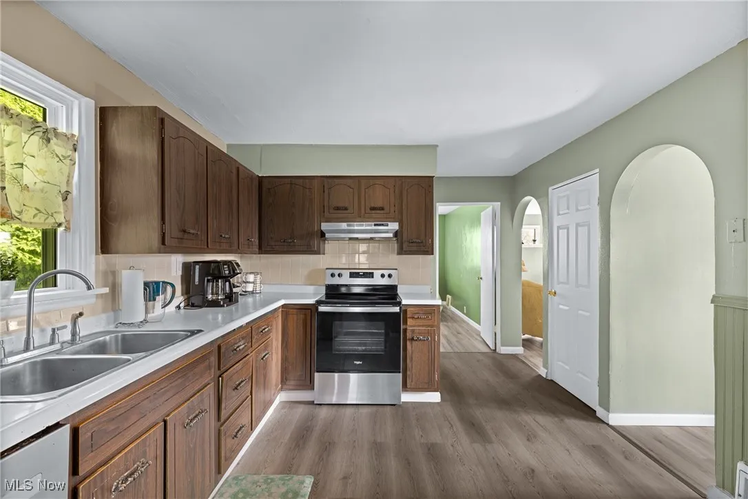 Kitchen with stainless steel range with electric stovetop, under cabinet range hood, a sink, and wood finished floors