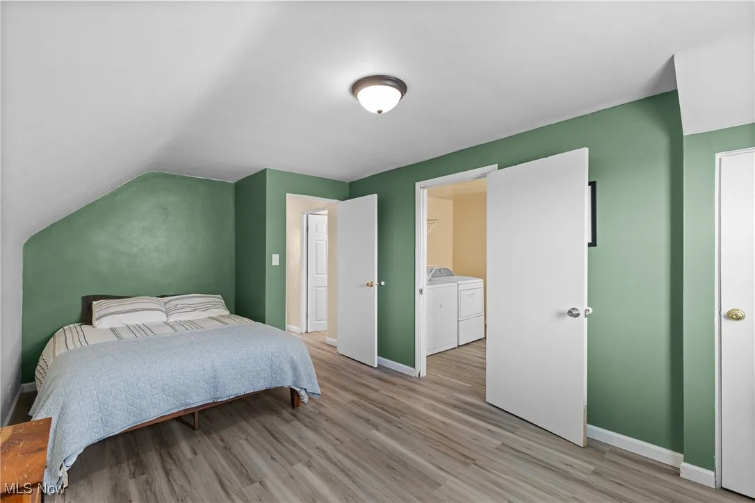 Bedroom featuring washer and dryer, light wood finished floors, baseboards, vaulted ceiling, and a spacious closet