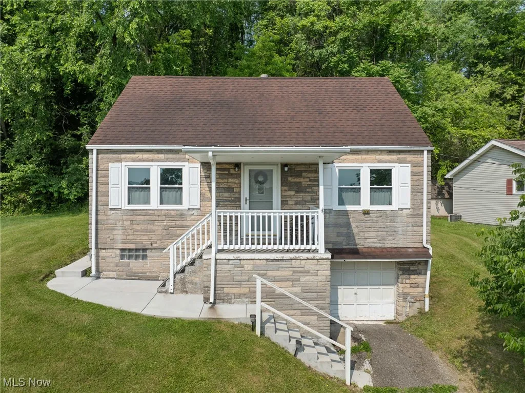 View of front of property featuring stone siding, a garage, a front yard, and asphalt driveway