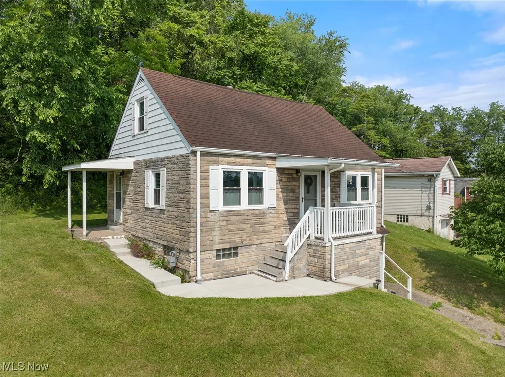 View of front of house with stone siding, a front yard, and roof with shingles