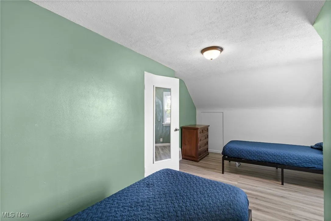 Bedroom featuring wood finished floors, vaulted ceiling, a textured ceiling, and baseboards