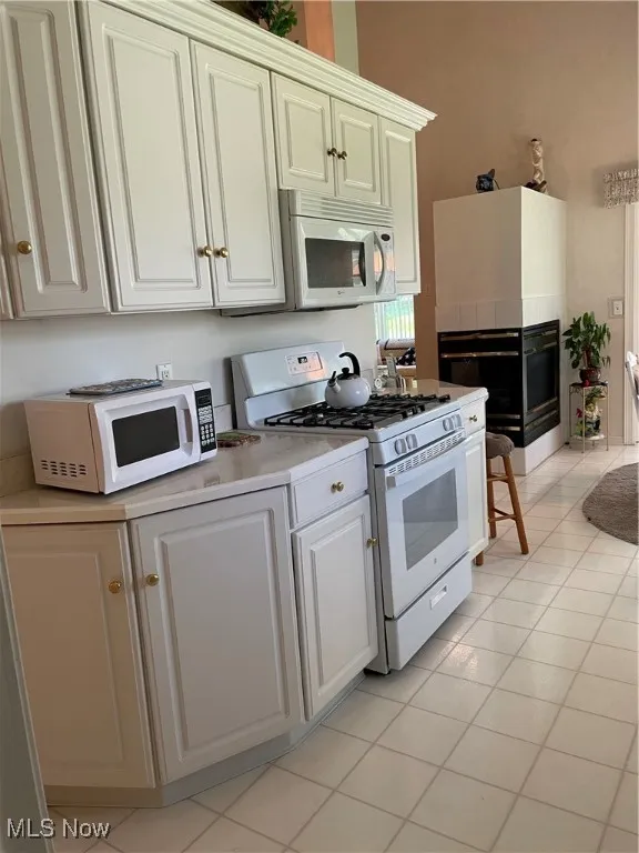 Kitchen featuring range, white microwave, a tile fireplace, light countertops, and light tile patterned floors