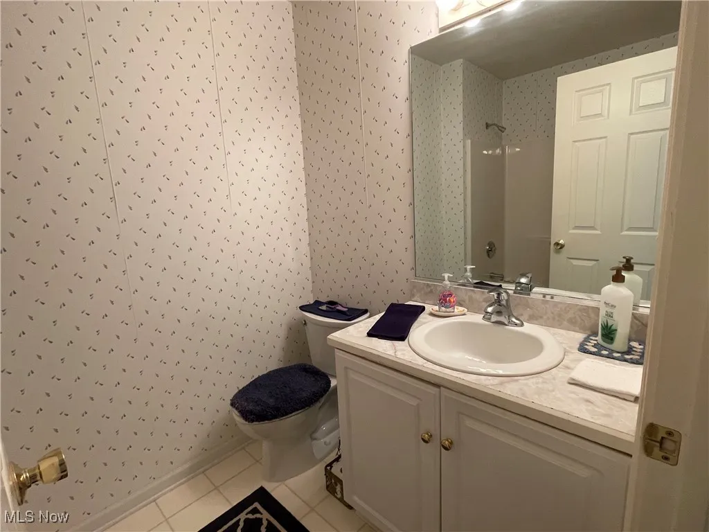 Bathroom with wallpapered walls, toilet, vanity, a shower, and tile patterned floors