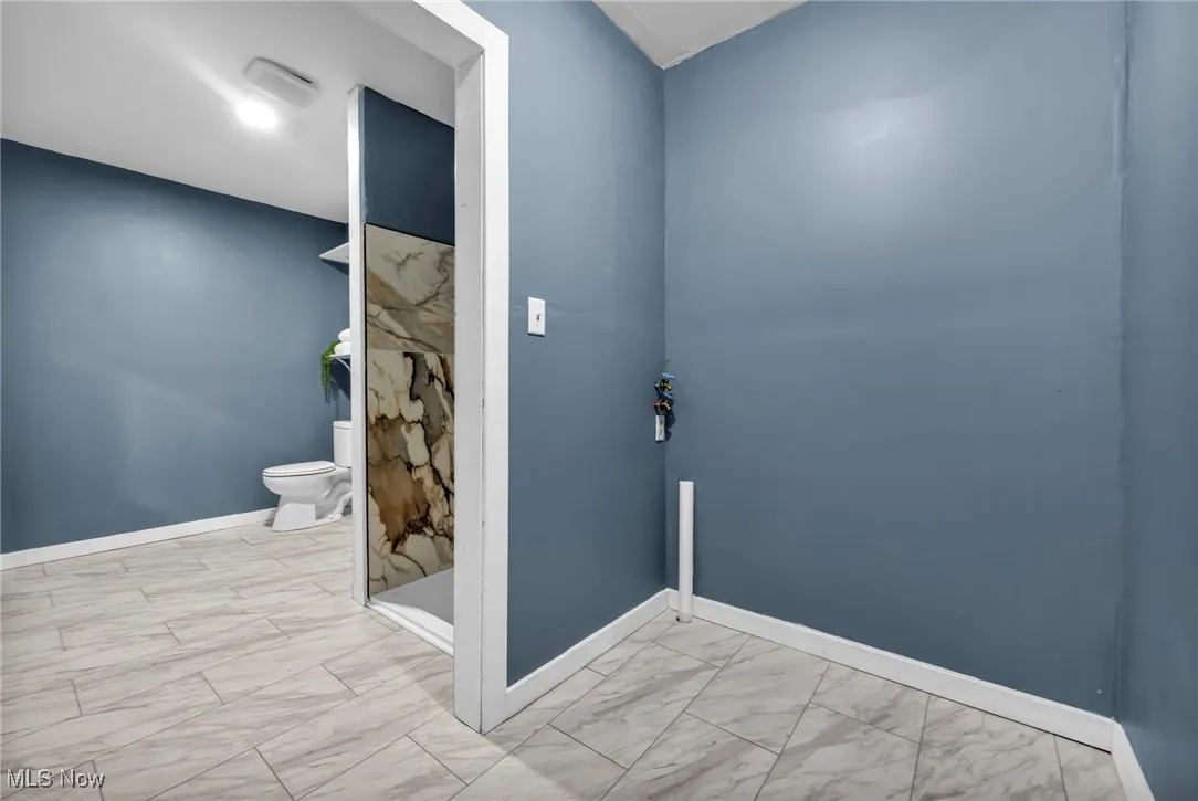 Full bathroom featuring marble look tiles, toilet, baseboards, and a walk in shower