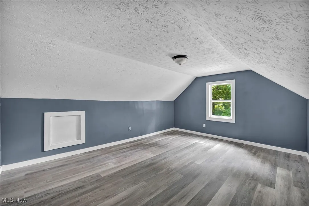 Additional living space with a textured ceiling, wood finished floors, baseboards, and vaulted ceiling