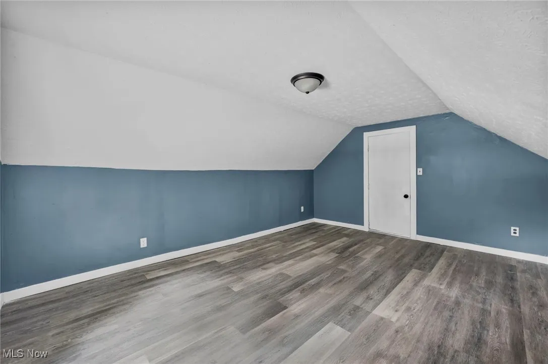 Additional living space featuring wood finished floors, vaulted ceiling, and baseboards