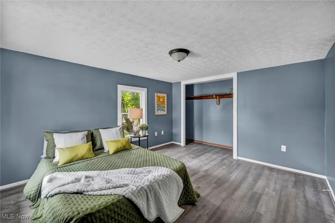 Bedroom with wood finished floors, baseboards, a closet, and a textured ceiling