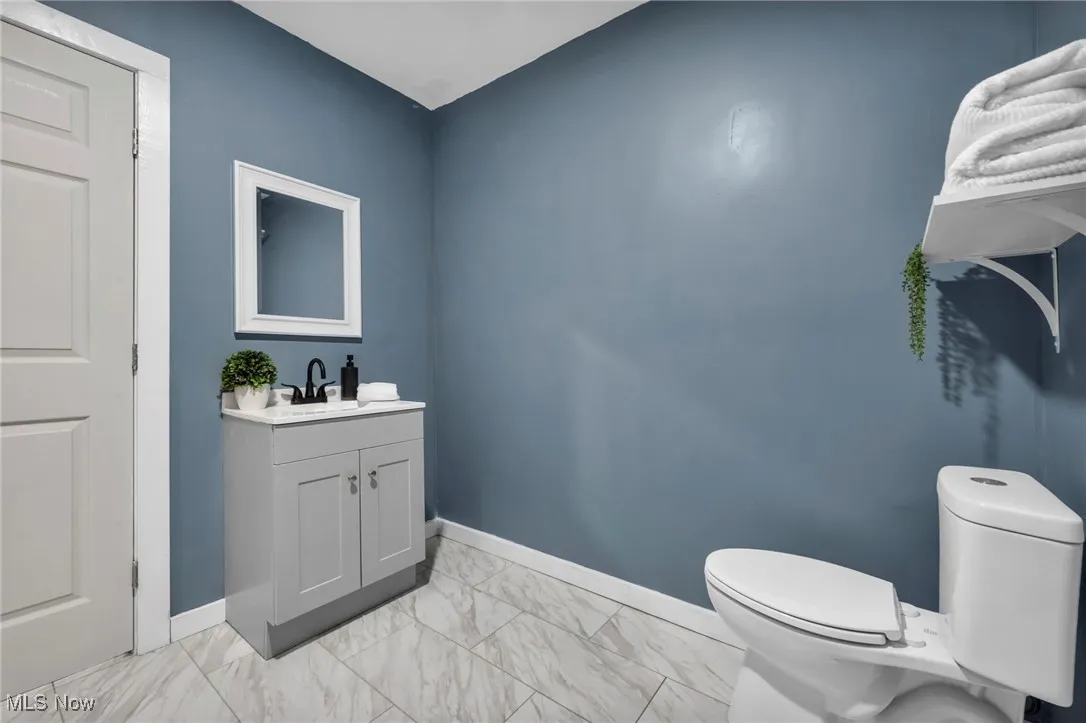 Bathroom with toilet, marble look tiles, vanity, and baseboards