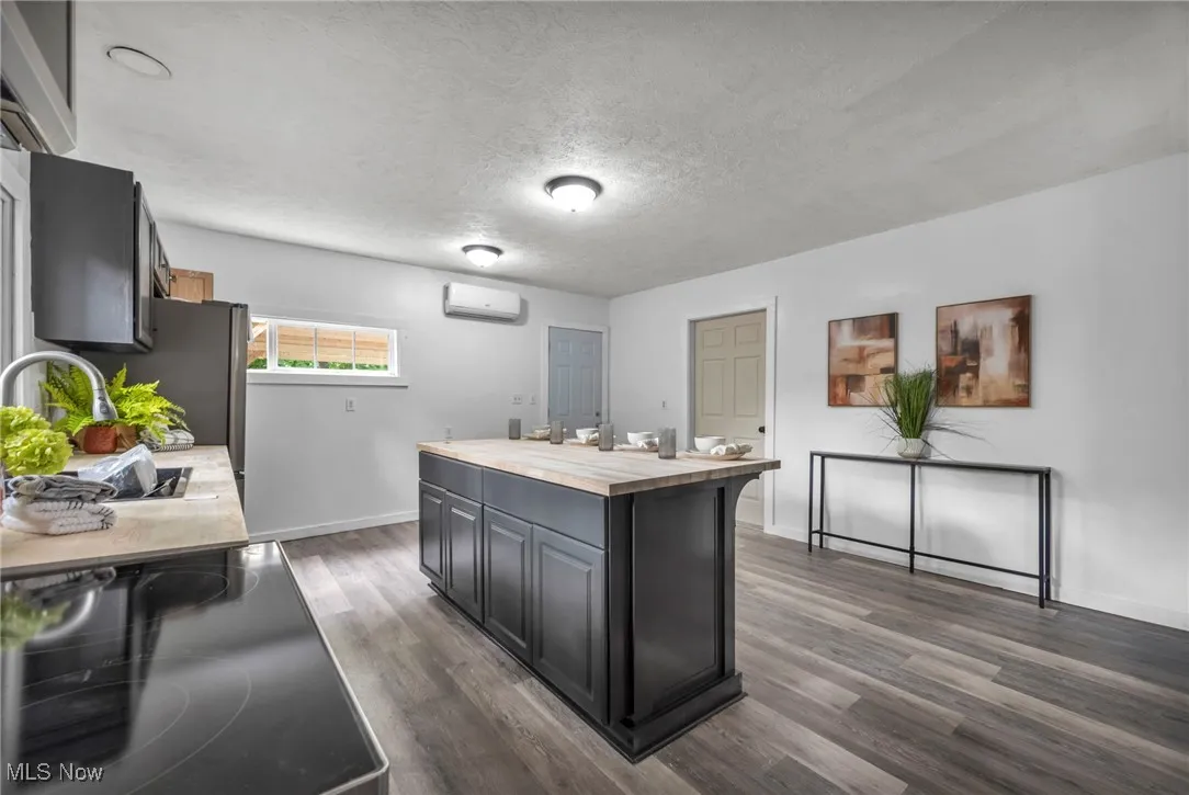 Kitchen with an AC wall unit, wooden counters, a sink, baseboards, and dark wood-style flooring