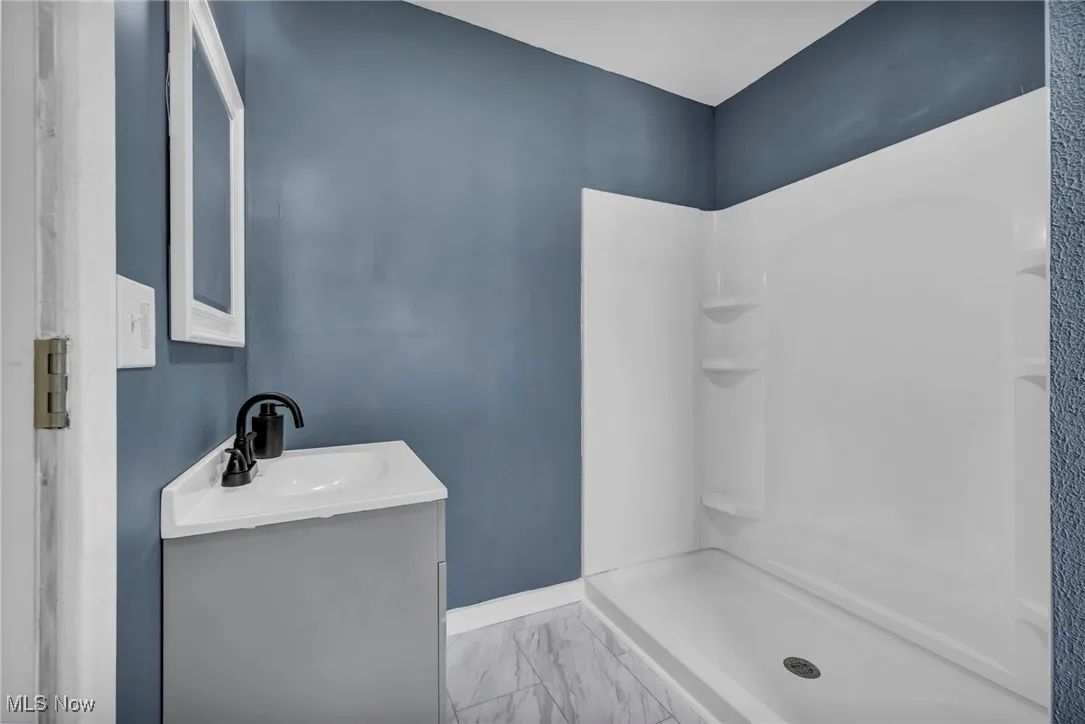 Full bathroom featuring vanity, a shower stall, marble look tiles, and baseboards