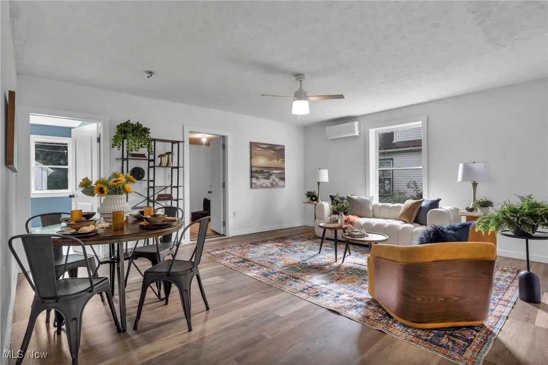 Living area with a wall mounted AC, wood finished floors, ceiling fan, baseboards, and a textured ceiling
