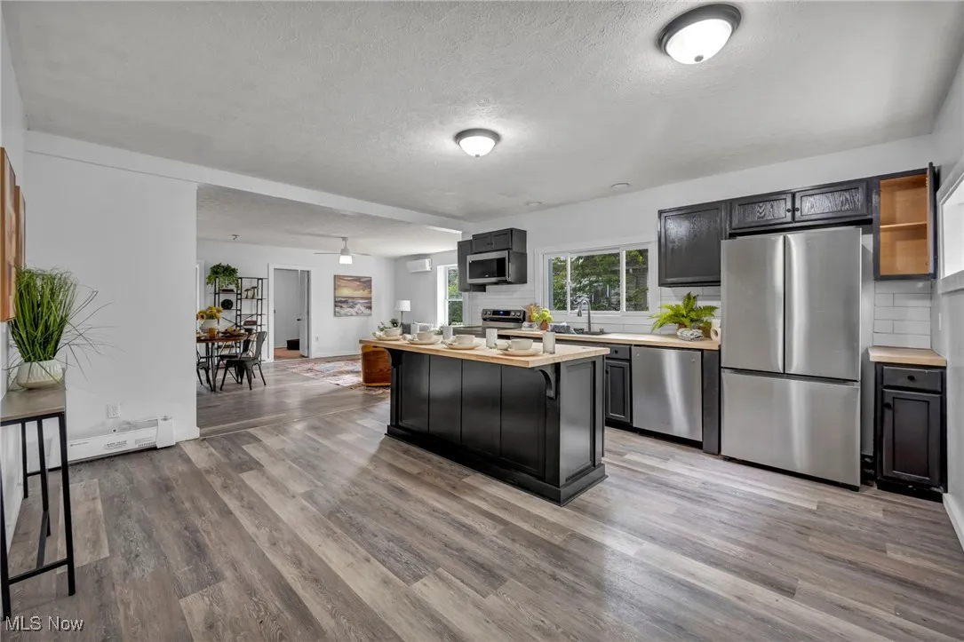 Kitchen featuring stainless steel appliances, a textured ceiling, wood finished floors, a breakfast bar area, and backsplash