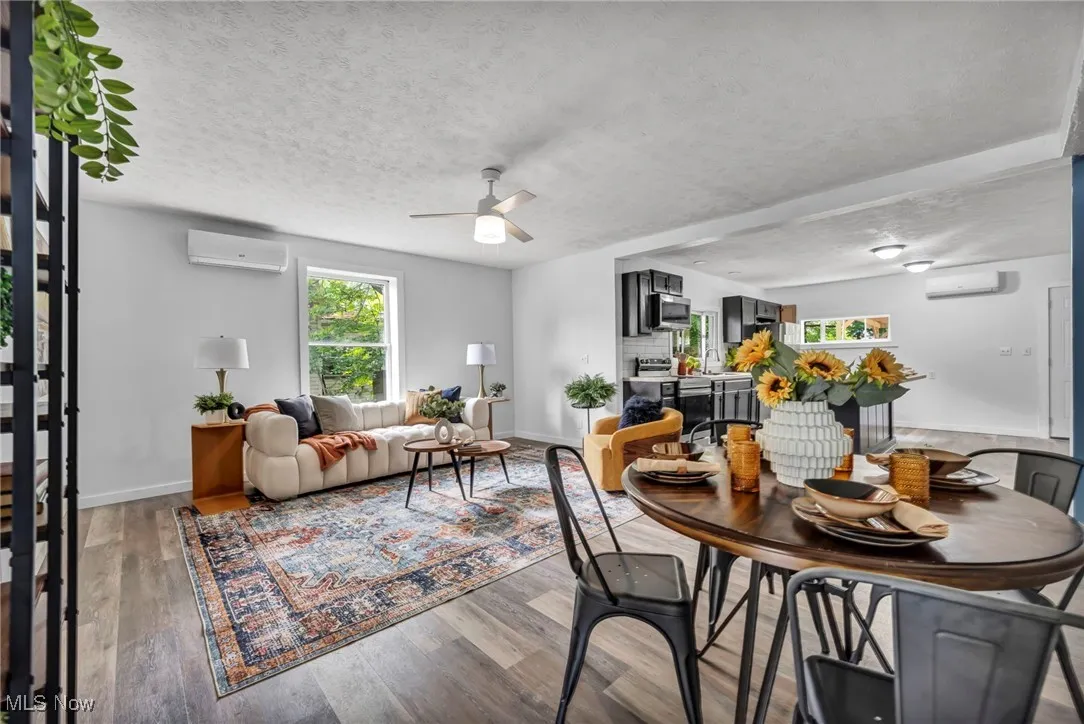 Dining area featuring a wall unit AC, a ceiling fan, light wood-style floors, a textured ceiling, and baseboards