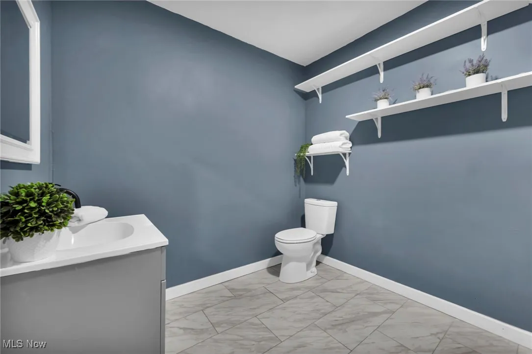 Bathroom featuring marble look tiles, vanity, toilet, and baseboards