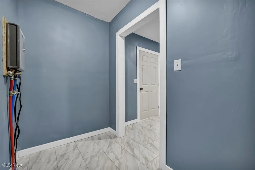 Corridor featuring marble look tile flooring and baseboards