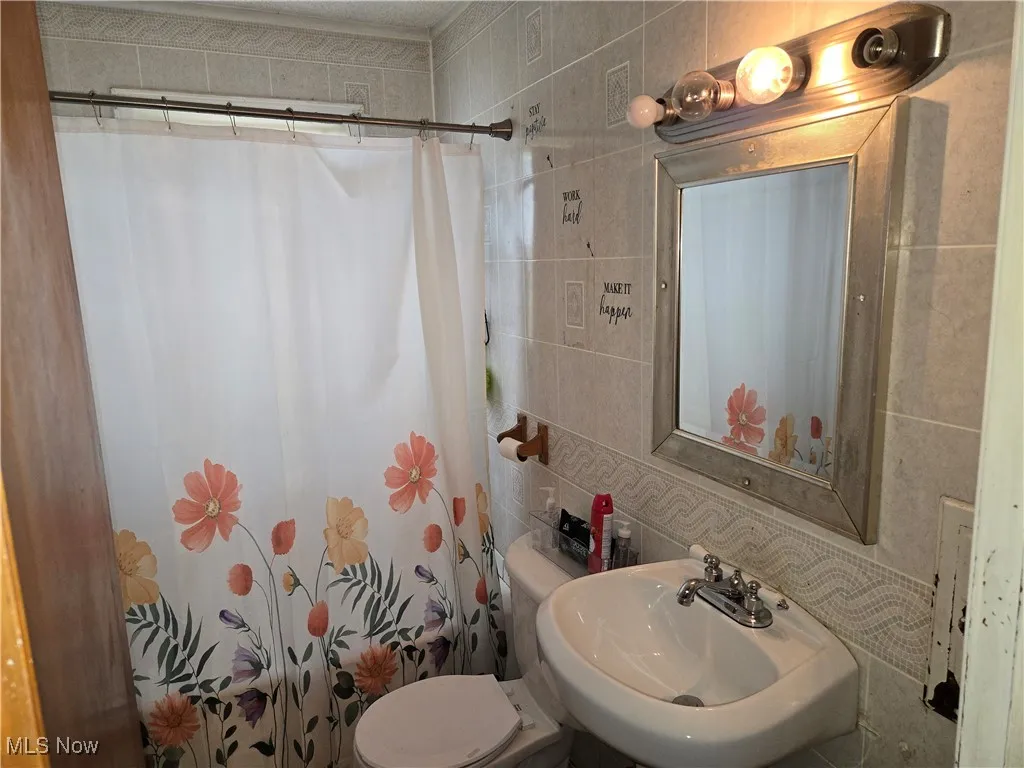 Bathroom featuring tile walls, toilet, curtained shower, decorative backsplash, and a sink