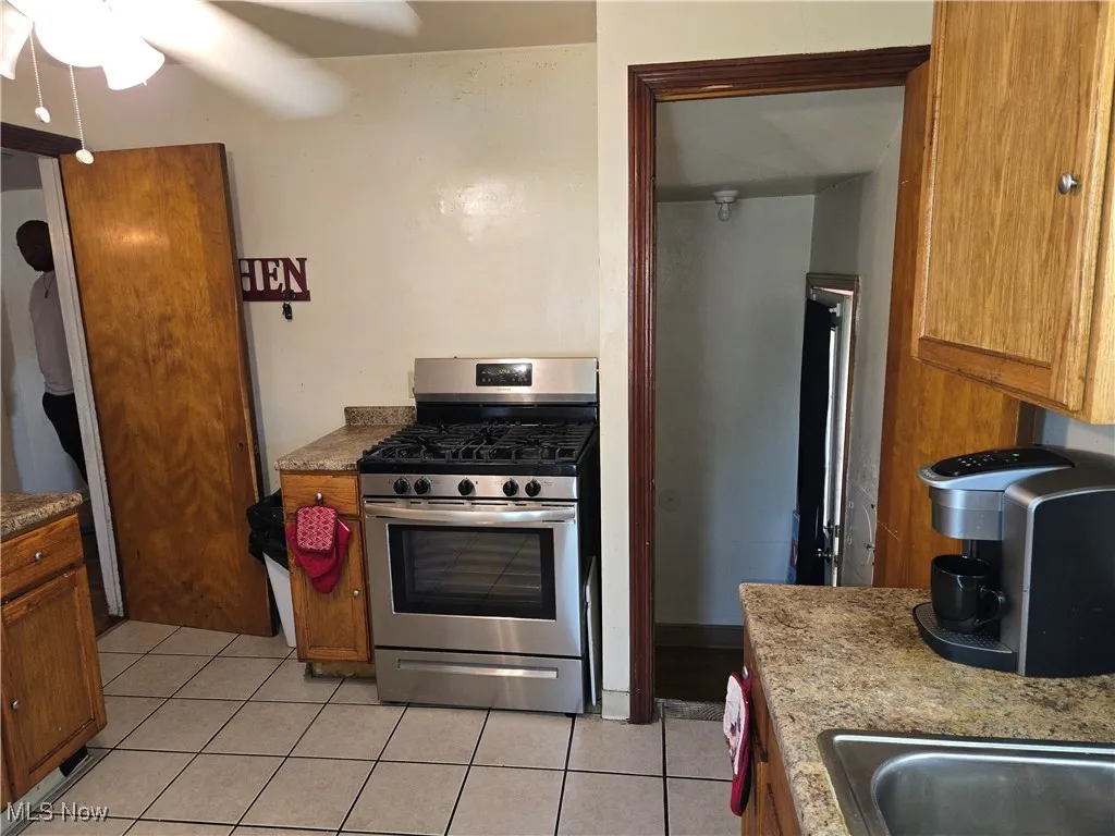 Kitchen featuring gas stove, light tile patterned flooring, ceiling fan, and brown cabinets