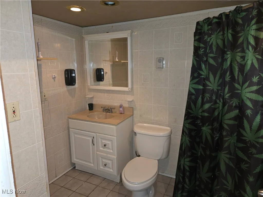 Bathroom with tile walls, tile patterned floors, toilet, vanity, and a shower with shower curtain