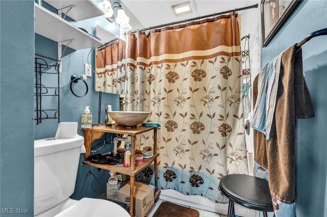 Full bath with toilet, curtained shower, a sink, and a textured wall