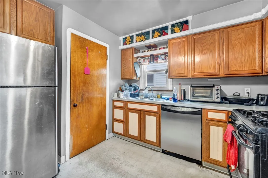 Kitchen featuring appliances with stainless steel finishes, light flooring, a sink, light countertops, and brown cabinetry