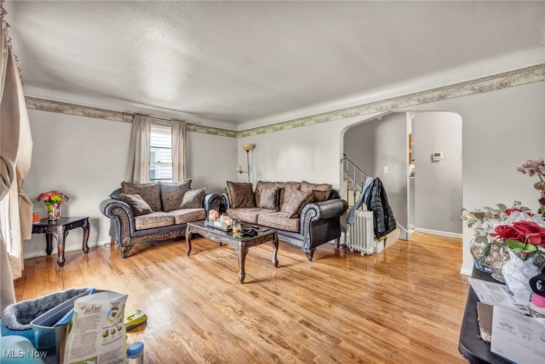 Living room with arched walkways, light wood-style floors, a textured ceiling, stairway, and baseboards