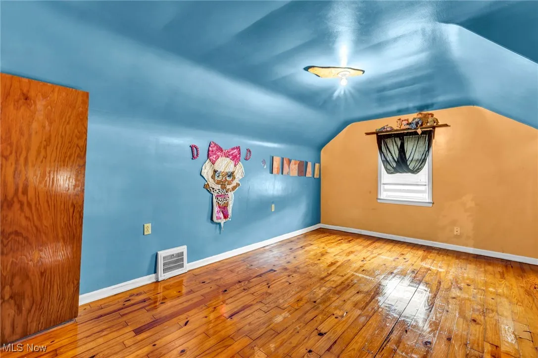 Additional living space with hardwood / wood-style flooring, vaulted ceiling, and baseboards
