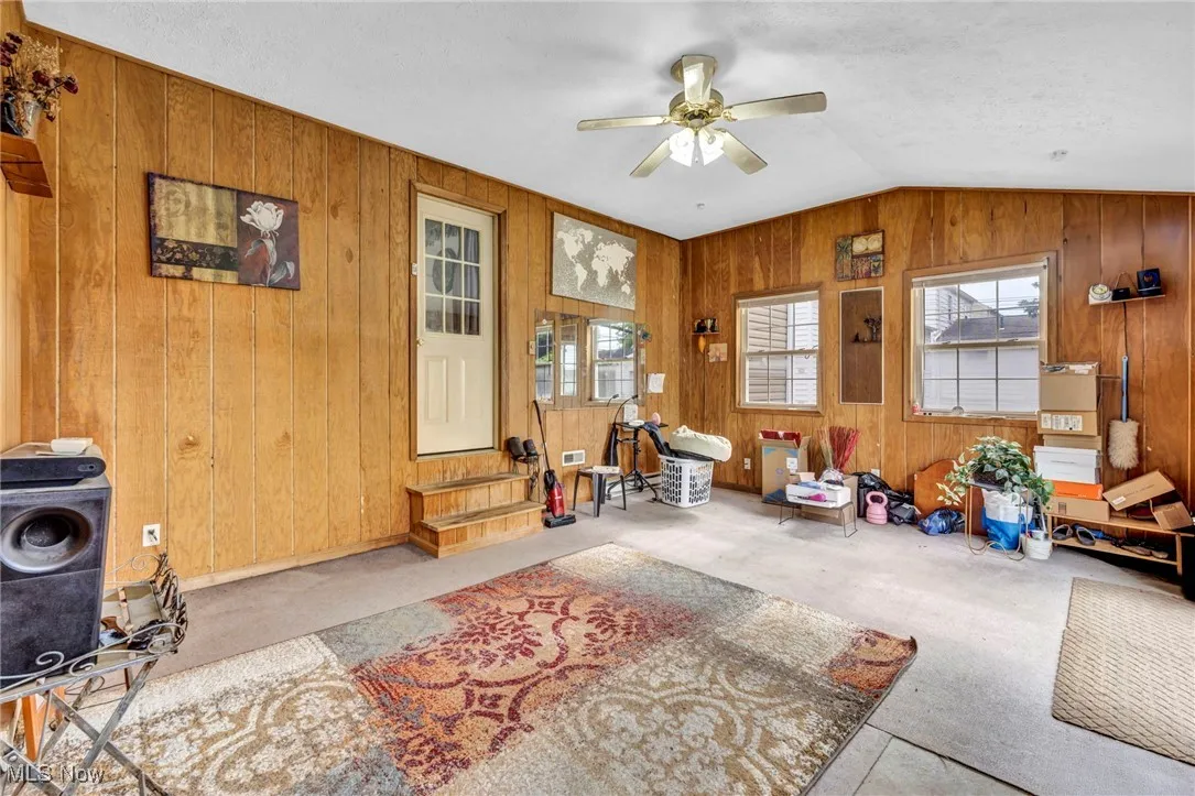 Carpeted bonus room with ceiling fan, wooden walls, and vaulted ceiling