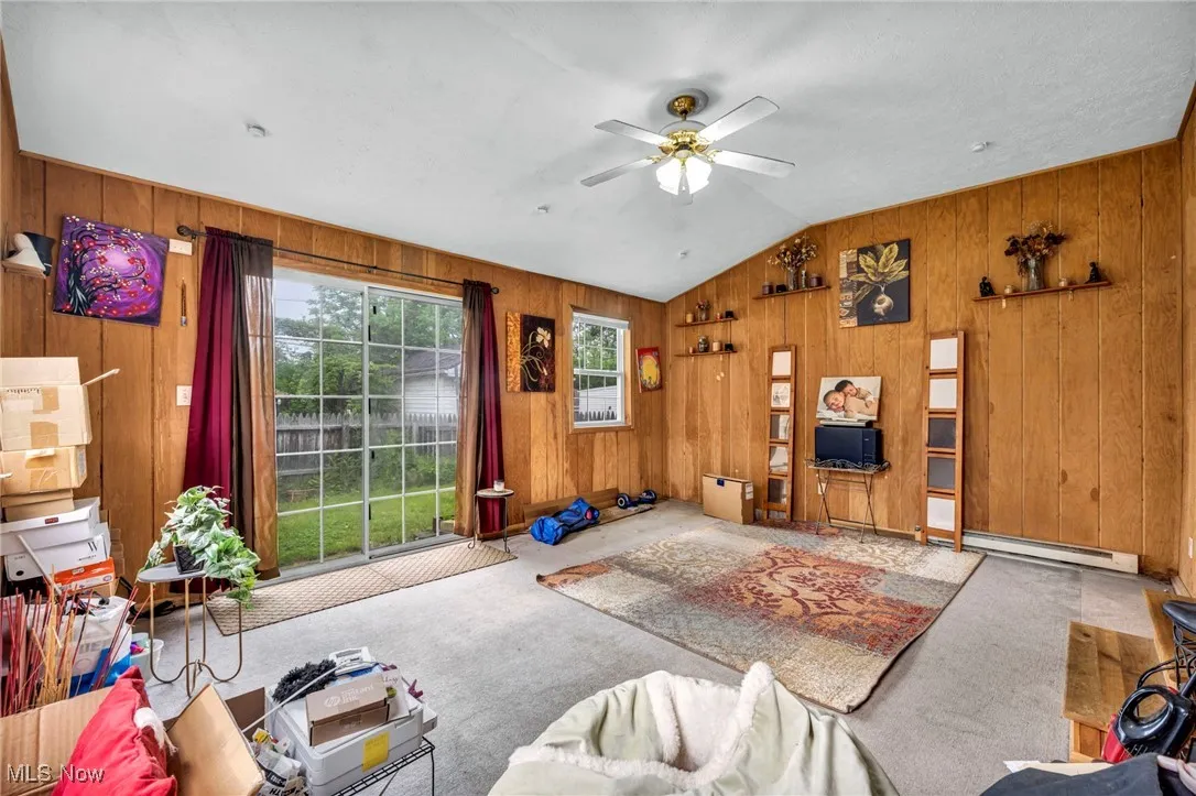 Carpeted bonus room with baseboard heating, ceiling fan, wood walls, and vaulted ceiling