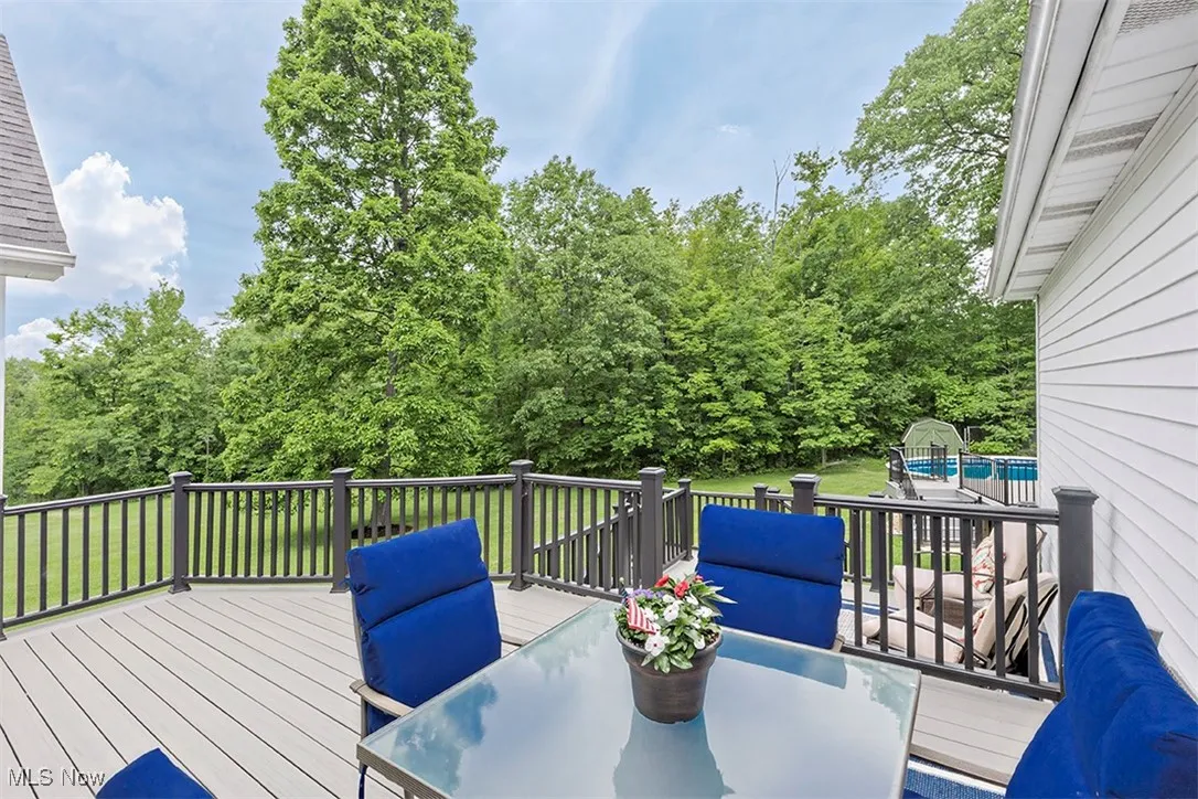 Rear deck overlooks groomed lawn and bordered by lush trees. Note the pool behind the house.