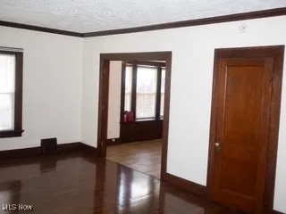 Spare room featuring healthy amount of natural light, wood finished floors, crown molding, and a textured ceiling