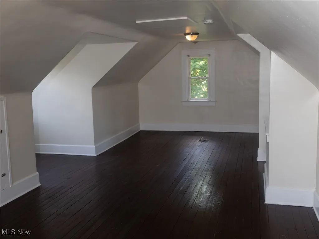 Bonus room with dark wood-style floors and lofted ceiling